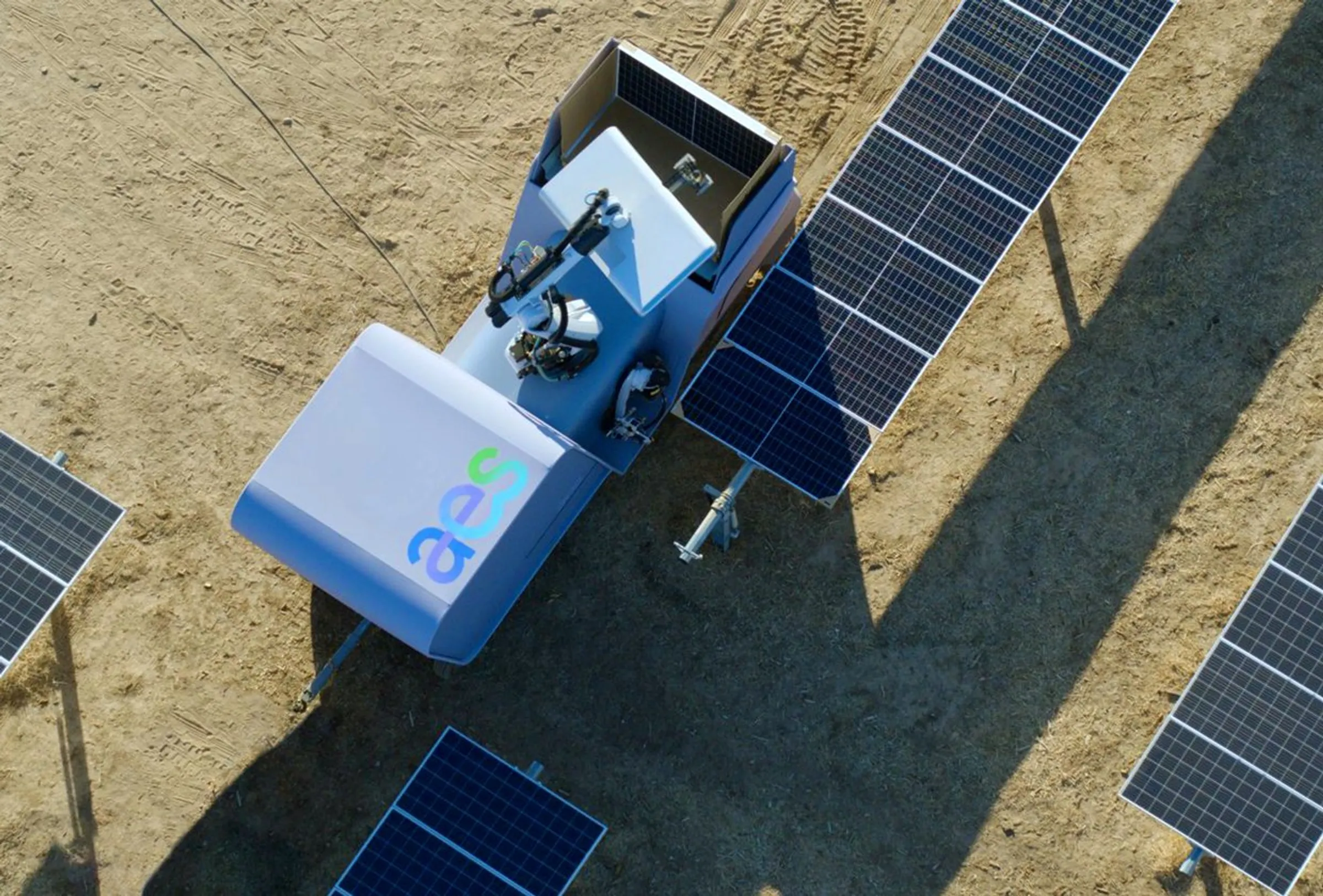 a-large-white-wheeled-robotic-vehicle-with-a-robotic-arm-next-to-solar-panels-in-a-field